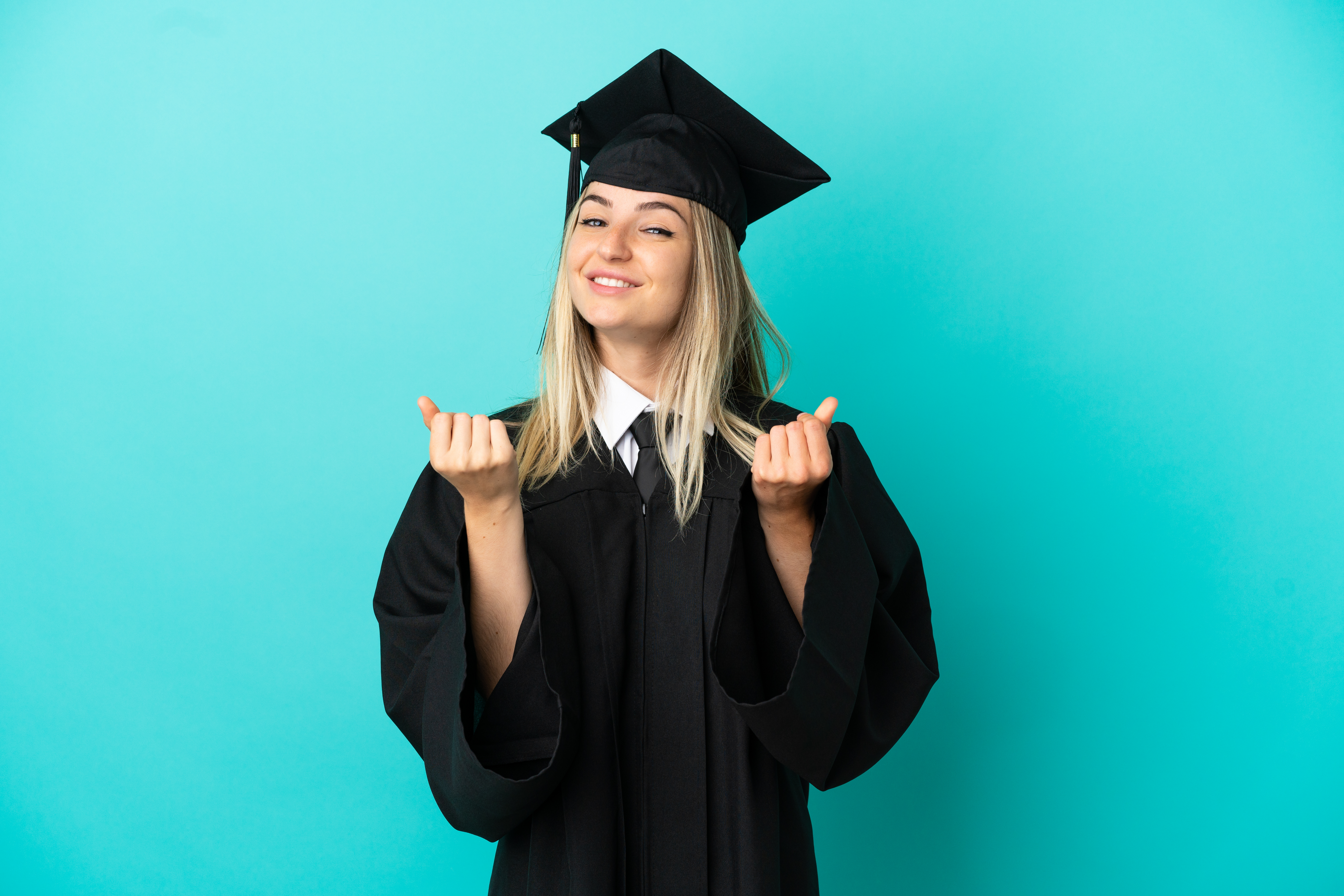 Young university graduate over isolated blue background making money gesture