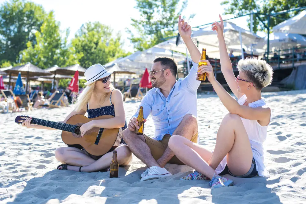 Three friends singing and drinking on the beach