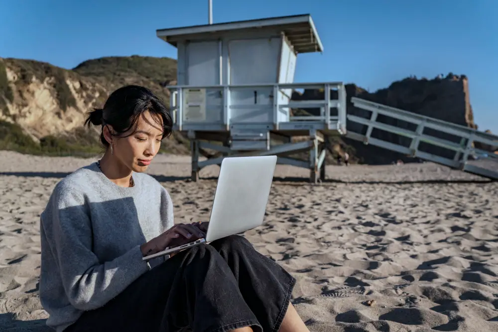 Young woman working on her laptop on the beach