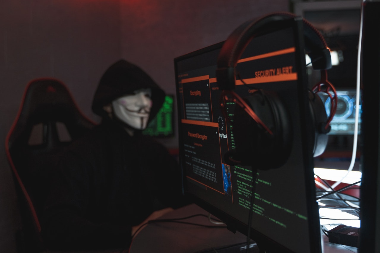masked hacker surrounded by computer screens