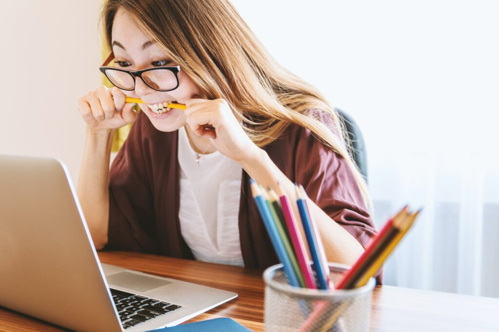 Asian woman bites on a pencil while looking at the laptop 