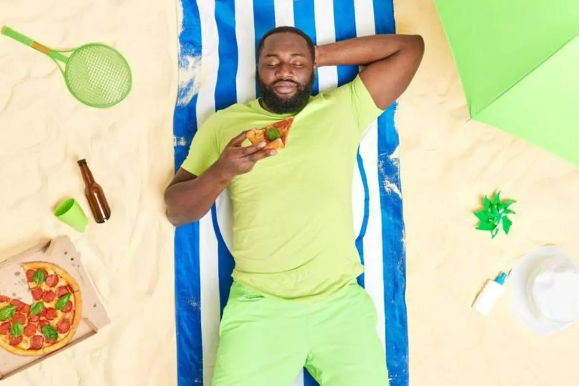 Man lies on the beach eating pizza