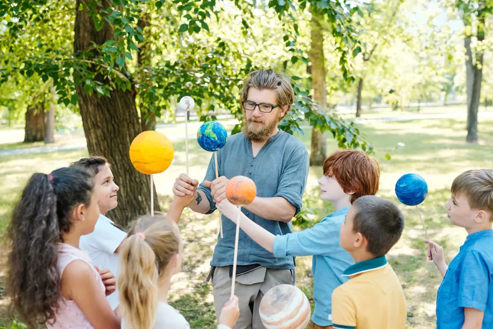 male-camp-counselor-teaching-crafts-to-kids-outdoors-during-summer-job