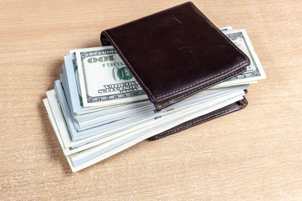 a huge stack of hundred dollar bills wedged inside a small brown leather wallet