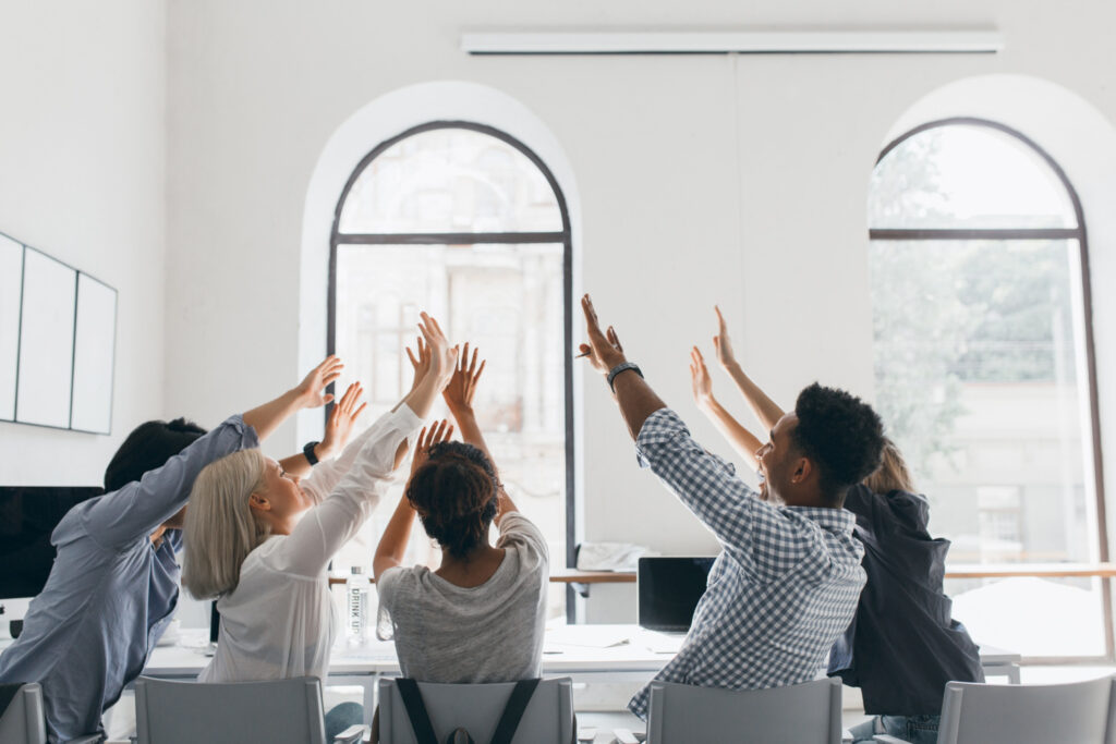 colleagues raising their hands to boost morale and develop a good working environment