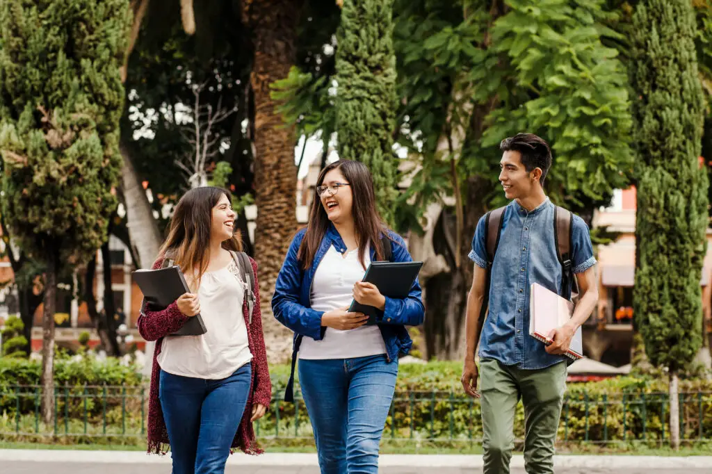 three-latin-american-undocumented-students-walking-on-leafy-campus-laughing