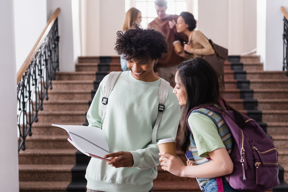 smiling-african-american-male-student-showing-notebook-to-female-student-at-ivy-league-college