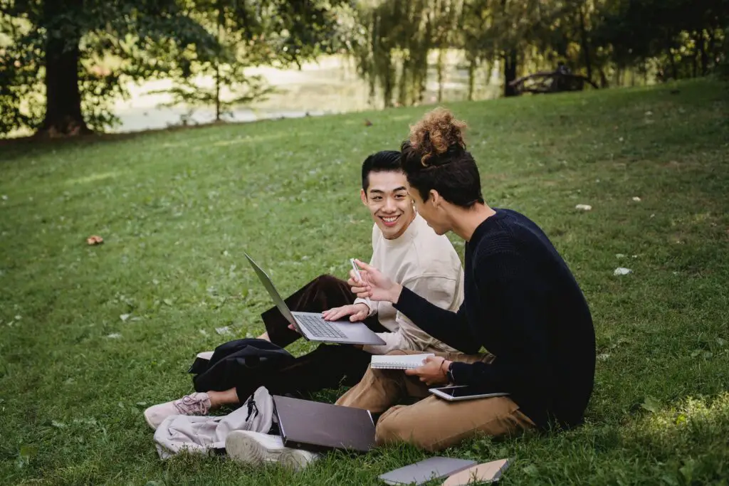 two-students-with-gadgets-talking-on-the-grass