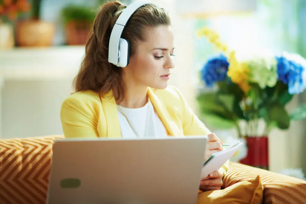 a-female-professor-wearing-headphones-is-using-Read-Aloud-Chrome-extension-while-writing-notes-on-a-notebook