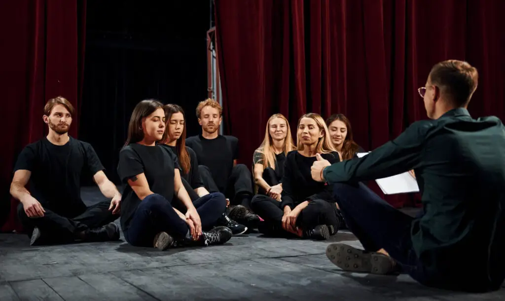 A group of seated theater college students listening to acting coach 