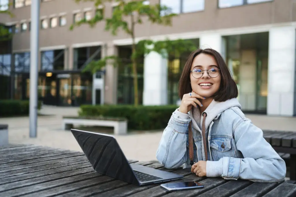 young-latina-girl-sits-outside-with-laptop-smiling-into-distance-thinking-about-being-accepted-into-ivy-league-college