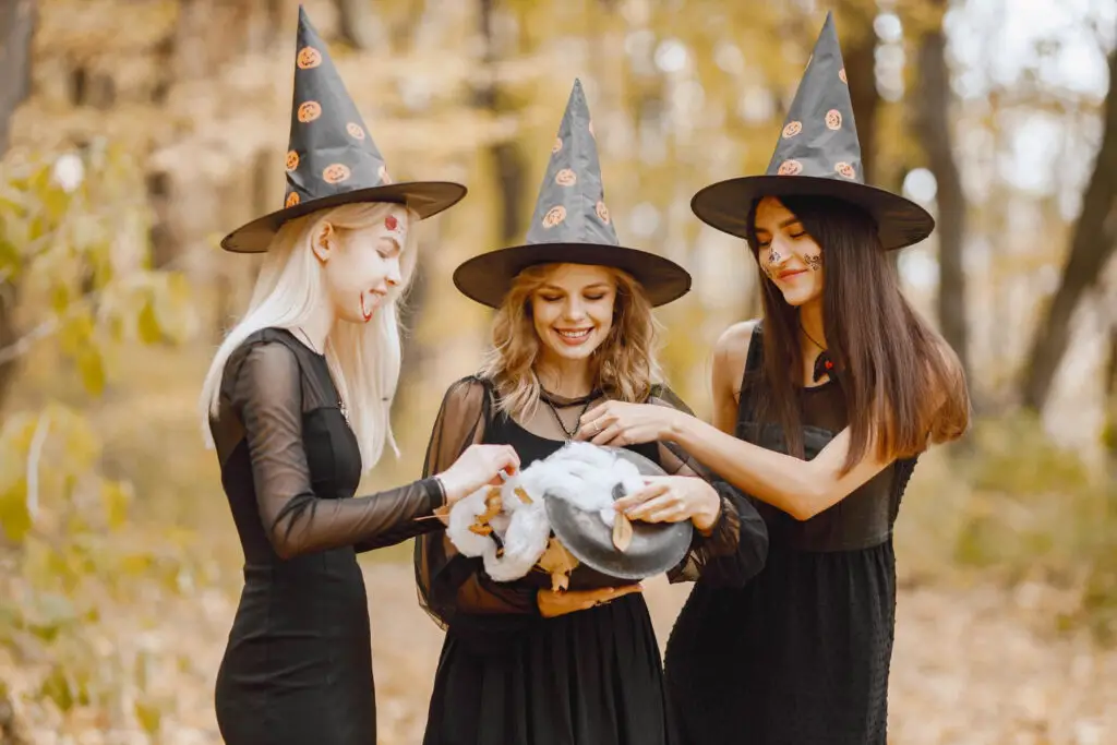 three-female-students-wearing-hats-and-dark-costumes-holding-a-cauldron-at-a-witches-and-wizards-college-party-theme