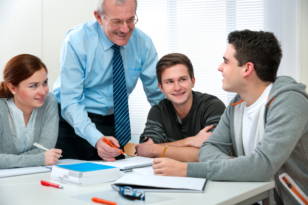 Three students in a small liberal arts college class discussing a lesson with their professor