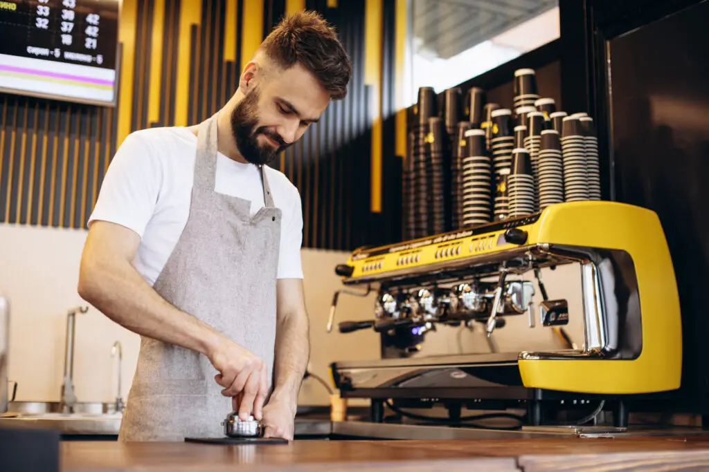 A college male tamping espresso in his part-time barista job