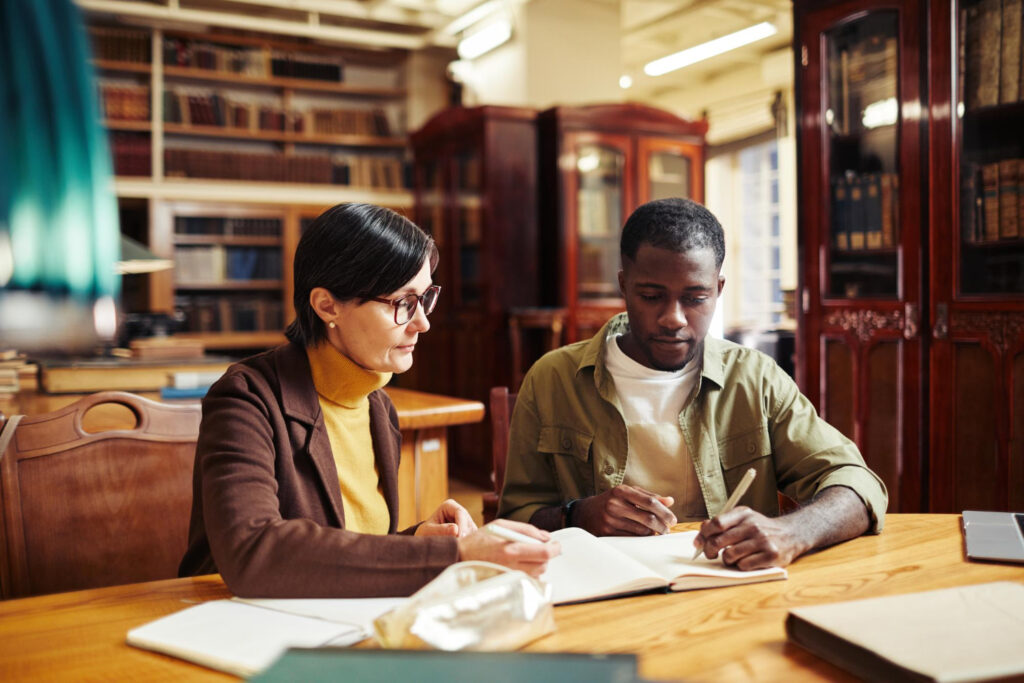 A female professor discussing her male student's narrative evaluation in a library