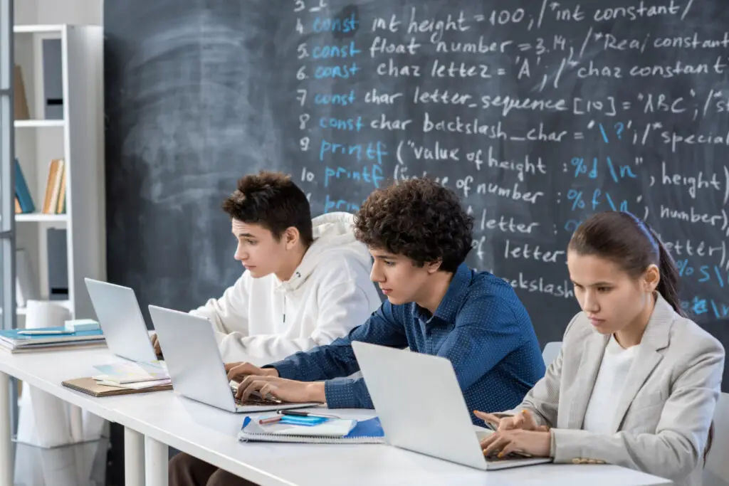 Three computer science college students coding on their laptops in the classroom