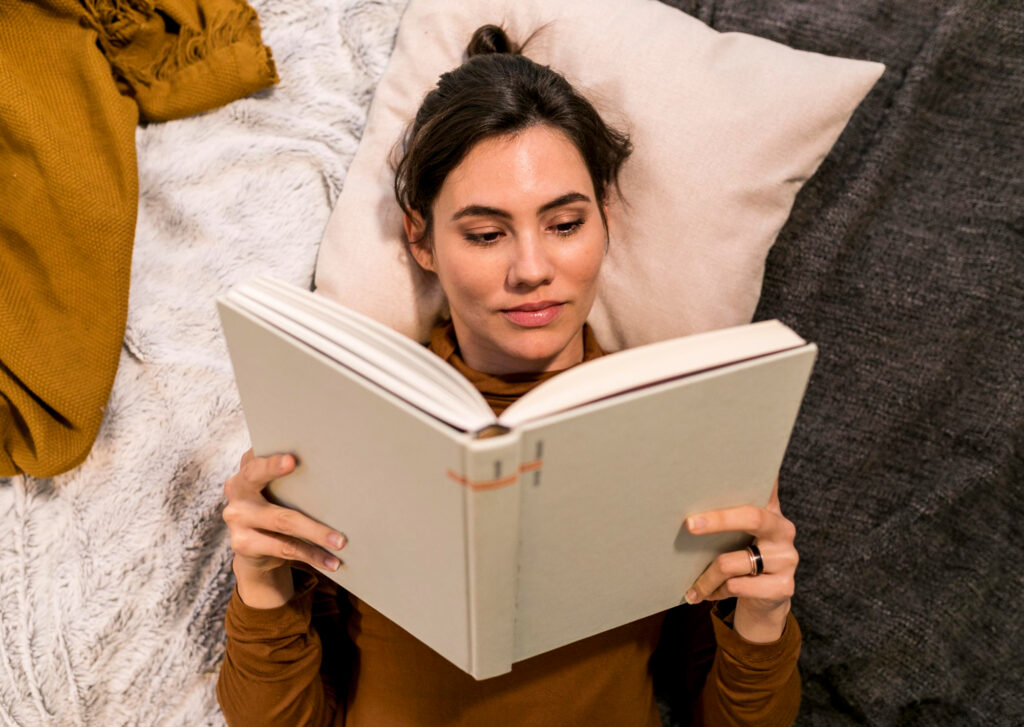 female-college-reading-a-book-in-bed-with-pillows-and-blanket-from-her-college-packing-checklist