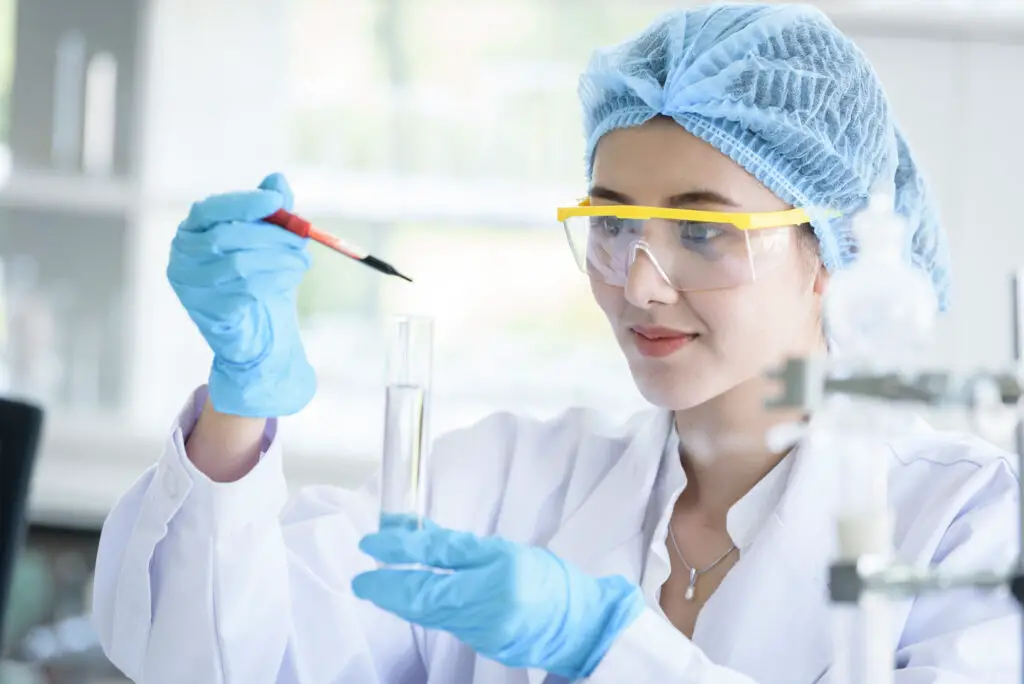 female medical student wearing eye goggles blue gloves and a white lab coat use Dailyrounds in studying chemistry and medicine