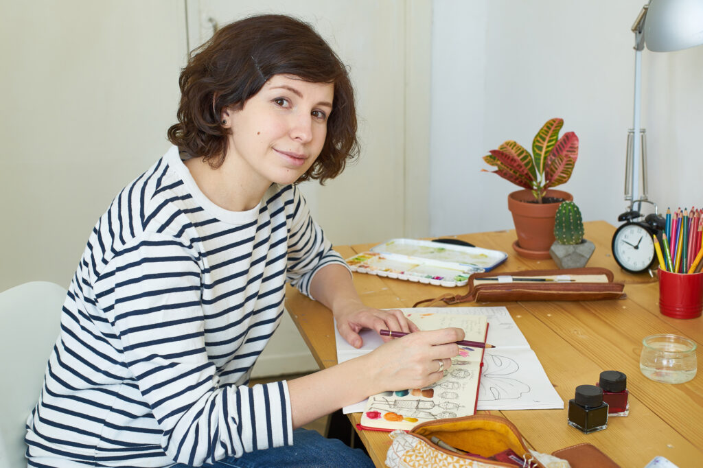 female-college-student-doing-artwork-at-her-desk-with-a-plant-lamp-and-art-supplies-from-her-college-packing-checklist-to-study-outdoors