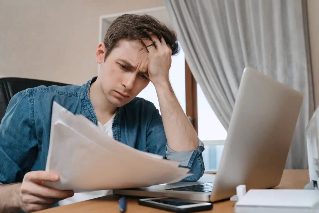 male-college-student-wearing-denim-shirt-reviewing-his-documents-to-ensure-he-avoids-the-common-FAFSA-mistake-of-using-incorrect-legal-information