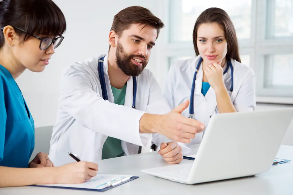 male and female medical students in blue scrubs and white lab gowns read about the latest medical news through the Medscape study tool on their laptop