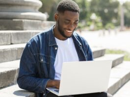 An African-American male college student typing a job application cover letter on his laptop outdoors