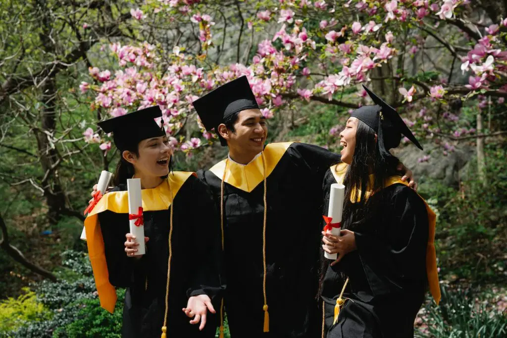 three-college-students-in-graduation-regalia-holding-diplomas-outdoors