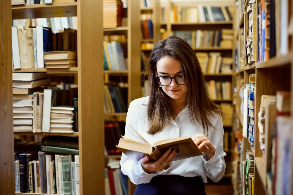 a-female-college-student-wearing-glasses-reading-in-a-library-for-her-English-major-class