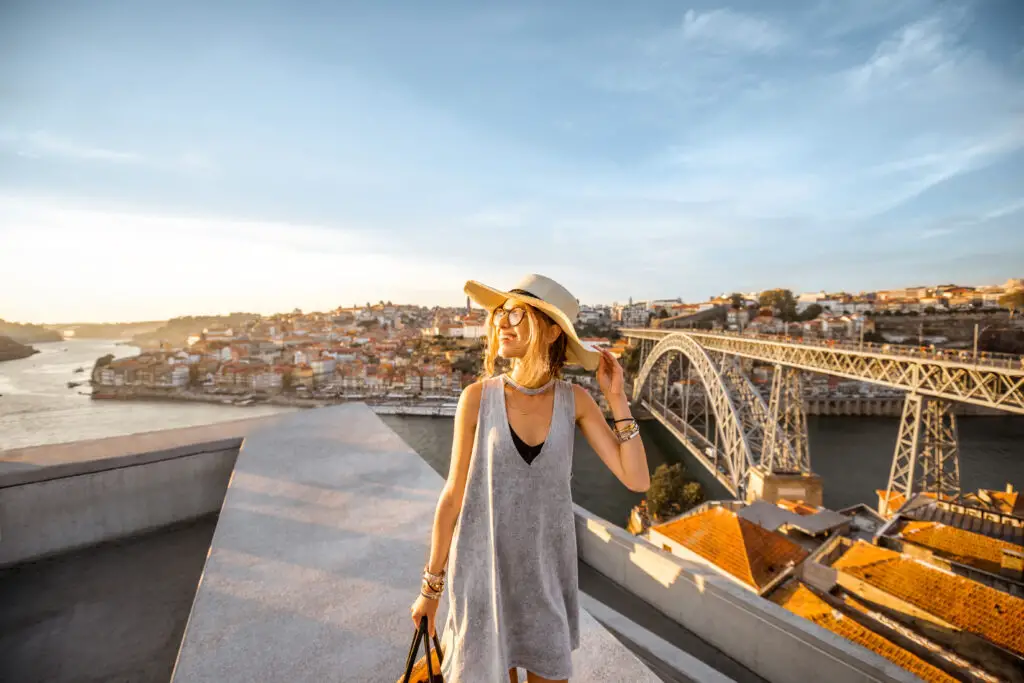 A smiling female college student poses for a photo during sunset at the Dom Luís I Bridge in Porto, Portugal