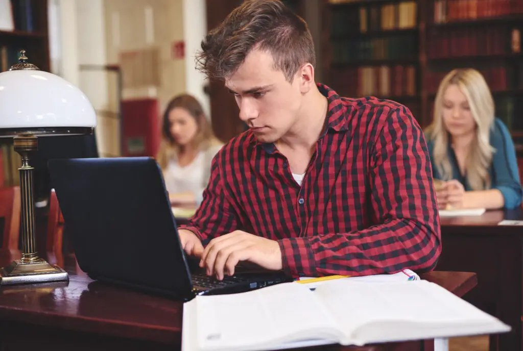 An American male college student using his laptop to research an unfamiliar concept while studying in the college library