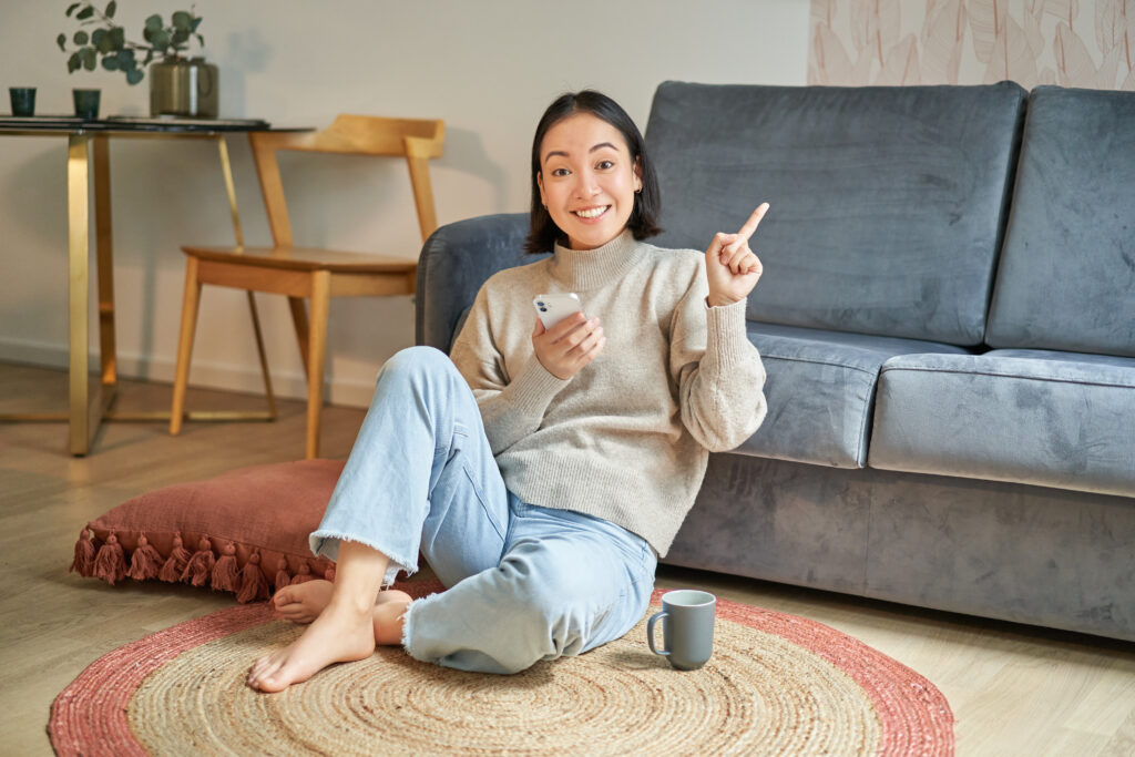 A smiling Asian female college student relaxing while scrolling on her phone after completing her studies for the day