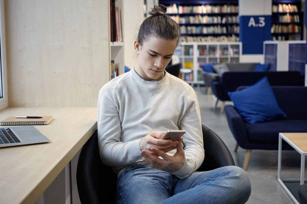 A Caucasian male college student quickly messages groupmates without getting distracted on his phone due to installed app blockers