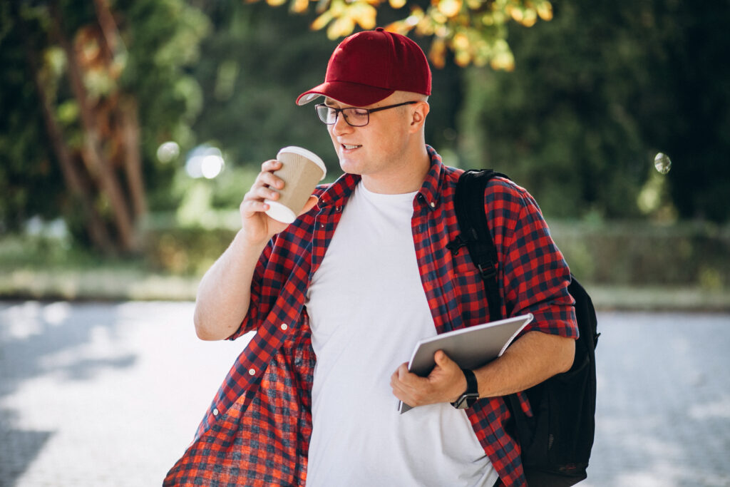 A male college student sips coffee to keep himself focused during class instead of getting distracted by his phone 