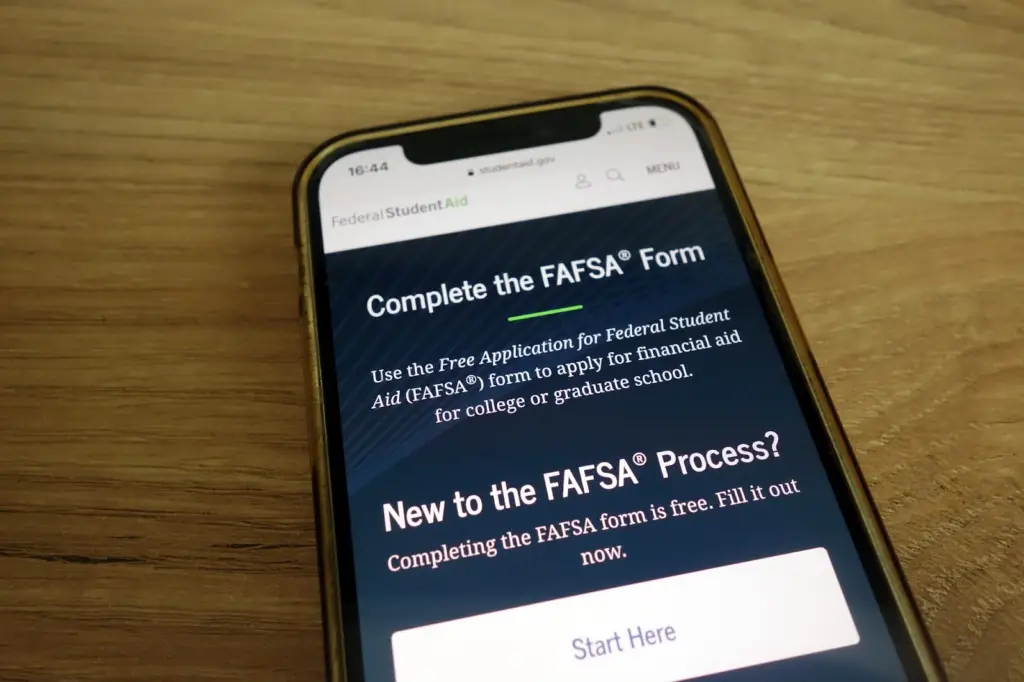 a mobile phone on a wooden desk features a screenshot of the online FAFSA application form
