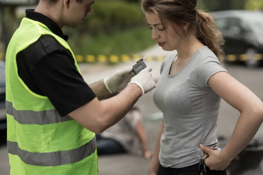 a female international college student=nt doing a breathalyzer test by a local enforcer wearing gloves and reflector neon vest