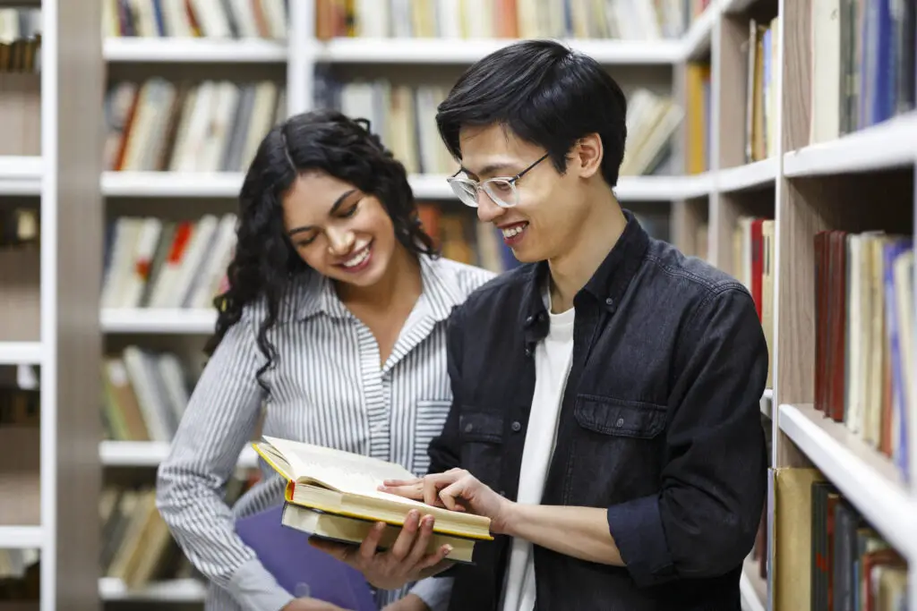 male and female international college students looking at books in a library that can be a supplemental reading for their course