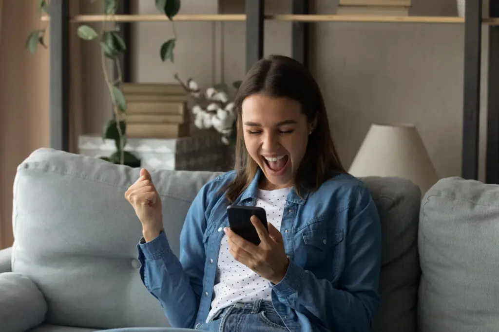 amazed-female-student-holding-smartphone-in-indoor-setup-yelling-in-delight