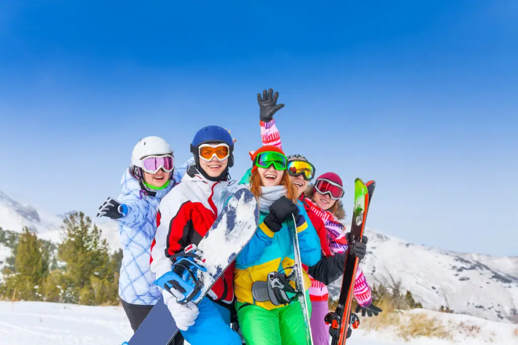 male and female college students holding snowboards and ski gear on to of a mountain slope
