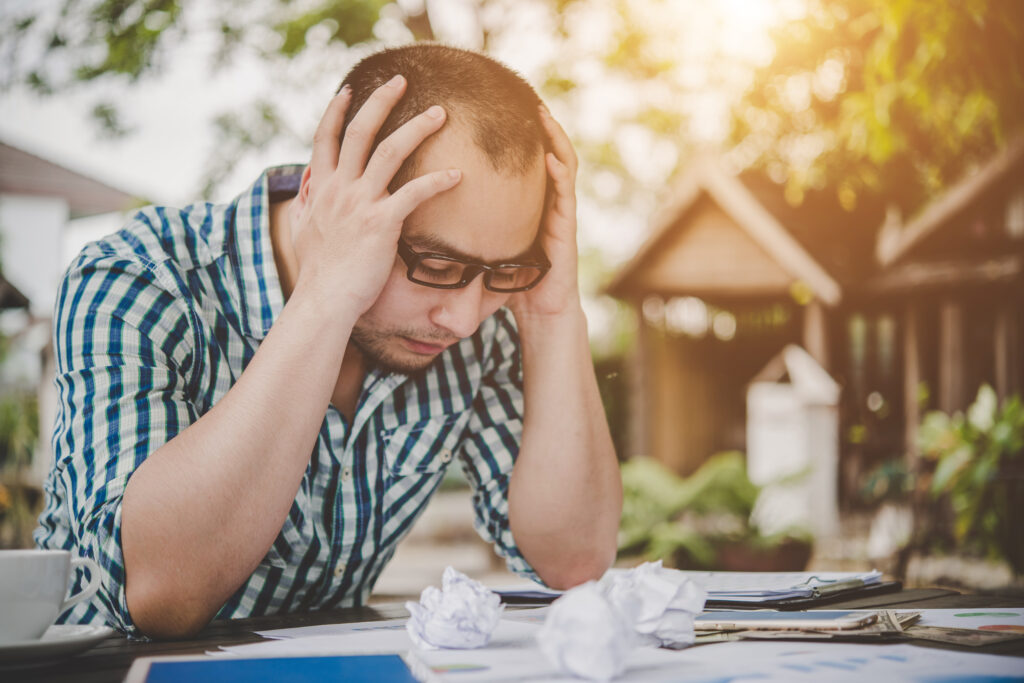 A male college student bows his head in frustration after calculating his student debts