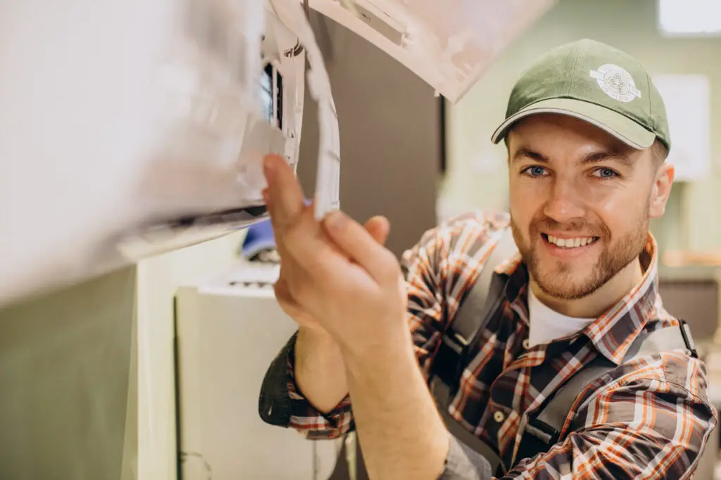 A smiling Caucasian male HVAC technician wearing a green cap and plaid polo at work 