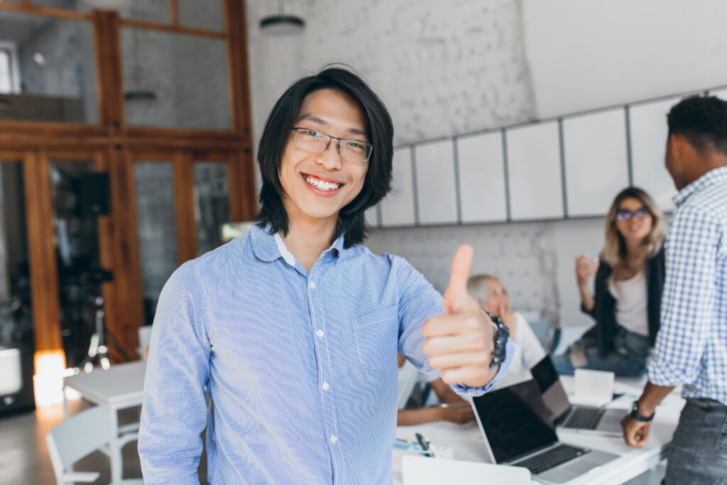 A smiling Asian male fresh college graduate giving a thumbs up review of his first job's salary
