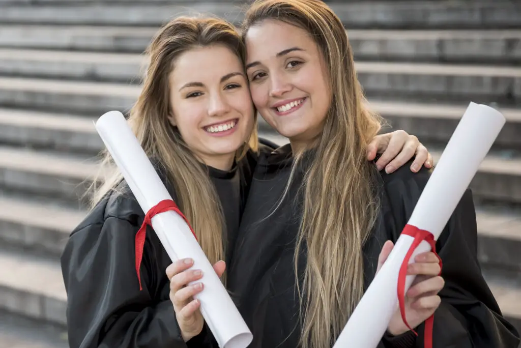 Two smiling Caucasian female high school graduates holding their diplomas