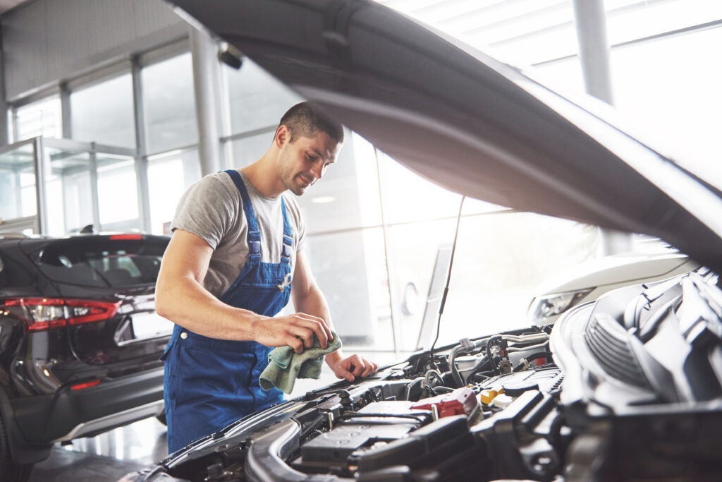 A smiling male automotive mechanic working on a car engine based on his training from trade school