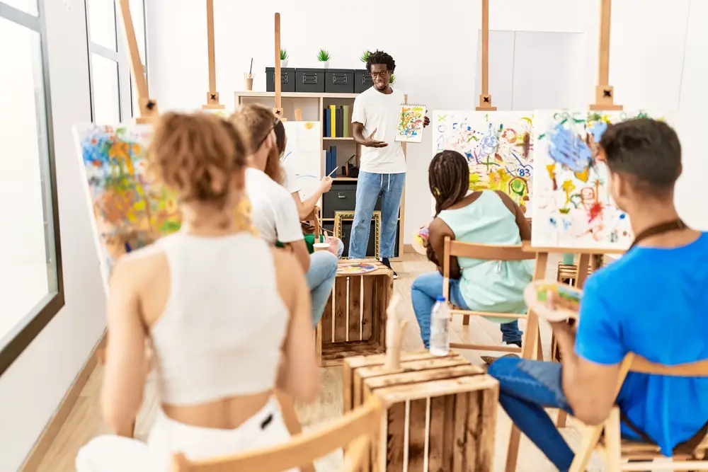 african-american-art-teacher-showing-a painting-to-a-group-of-students-at-an-art-studio
