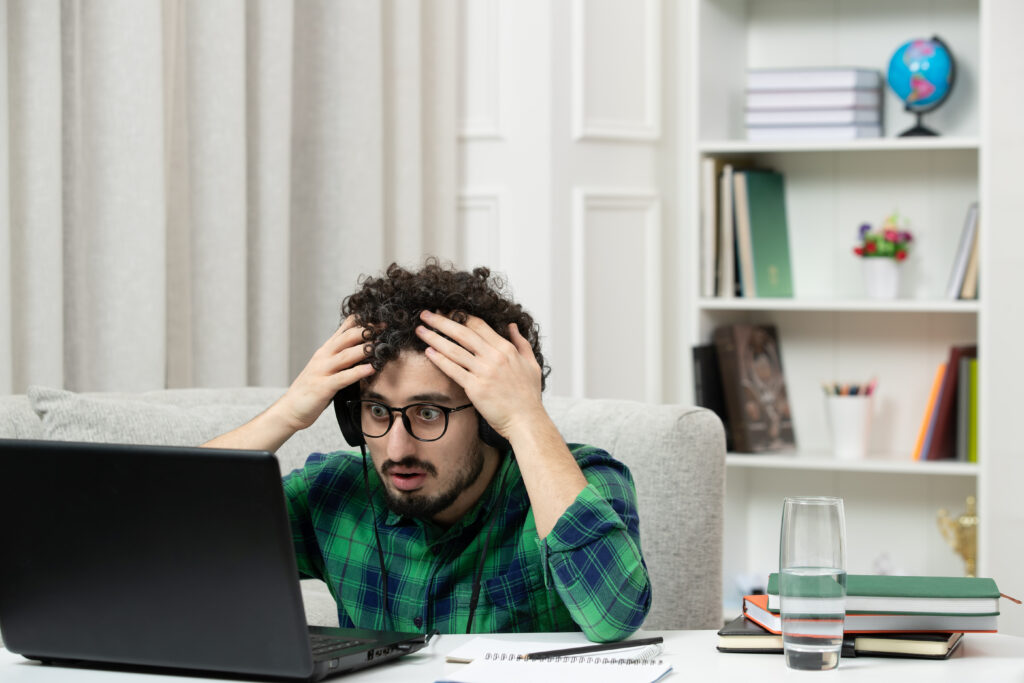 young-male-student-wearing-specs-looks-at-laptop-in-shock-holding-head