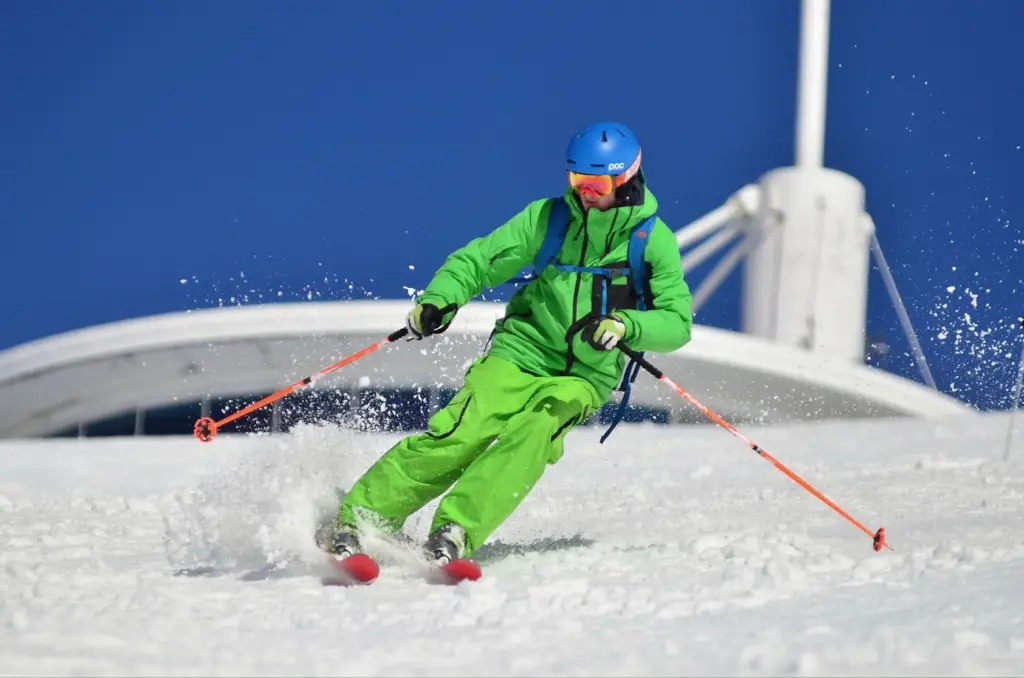 female college student wearing green winter gear skiing on a hill covered in snow