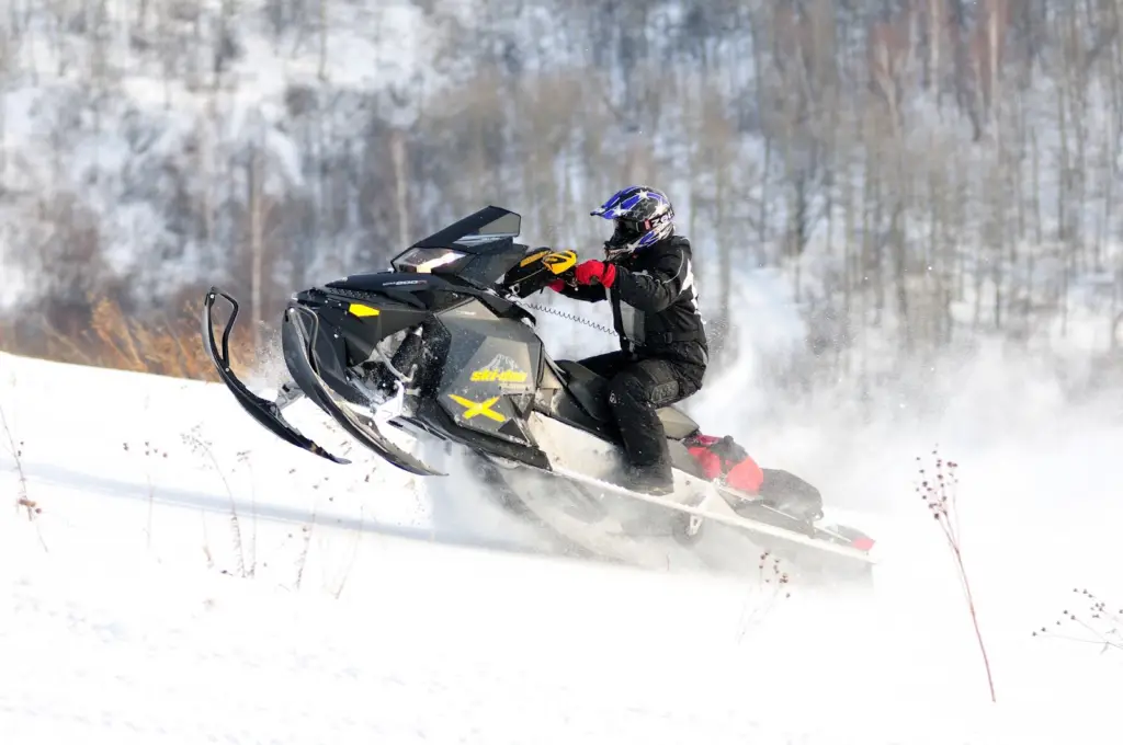 student attending the best US colleges for winter sports in black winter sports gear riding a snowmobile on a mountain slope