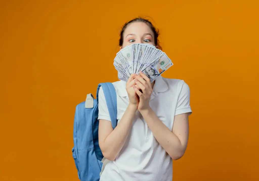young-female-student-with-backpack-against-orange-background-looking-at-wad-of-notes