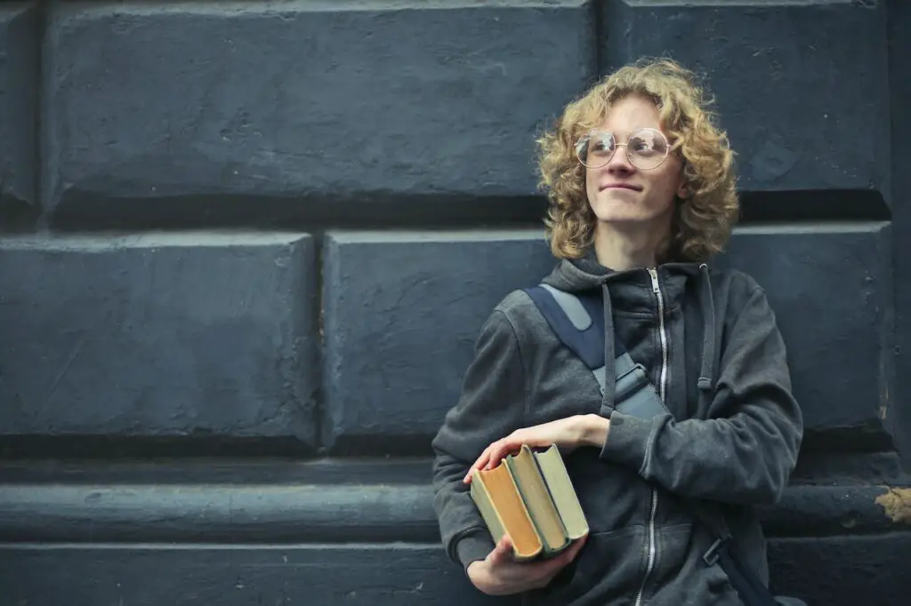 young-man-wearing-specs-leaning-against-a-wall-holding-books
