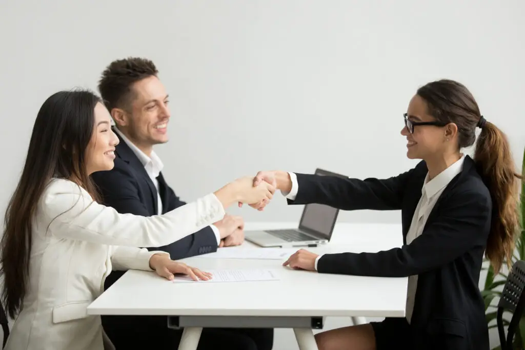 Two smiling corporate recruiters congratulating a female applicant during a job interview